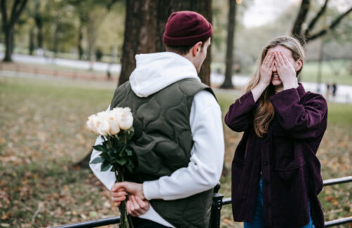 男性が背中に花束を隠している。女性が目を手で覆っている