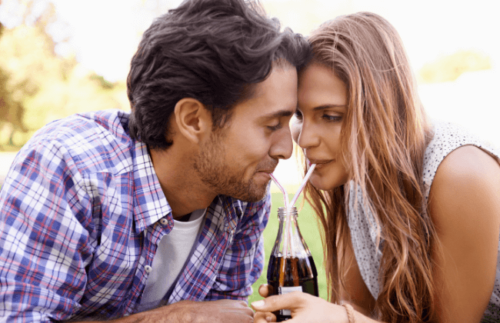 男性と女性が1本のコーラをストロー2つを使用しておでこをくっつけて飲んでいる
